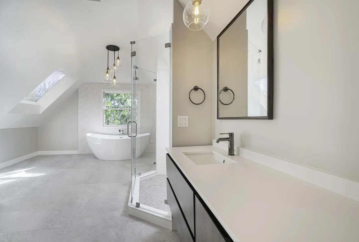 Master bathroom under a skylight with a freestanding tub, glass shower and floating vanity
